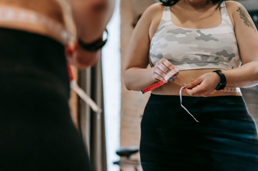 Low angle of crop faceless overweight female in activewear reflecting in mirror in sports club